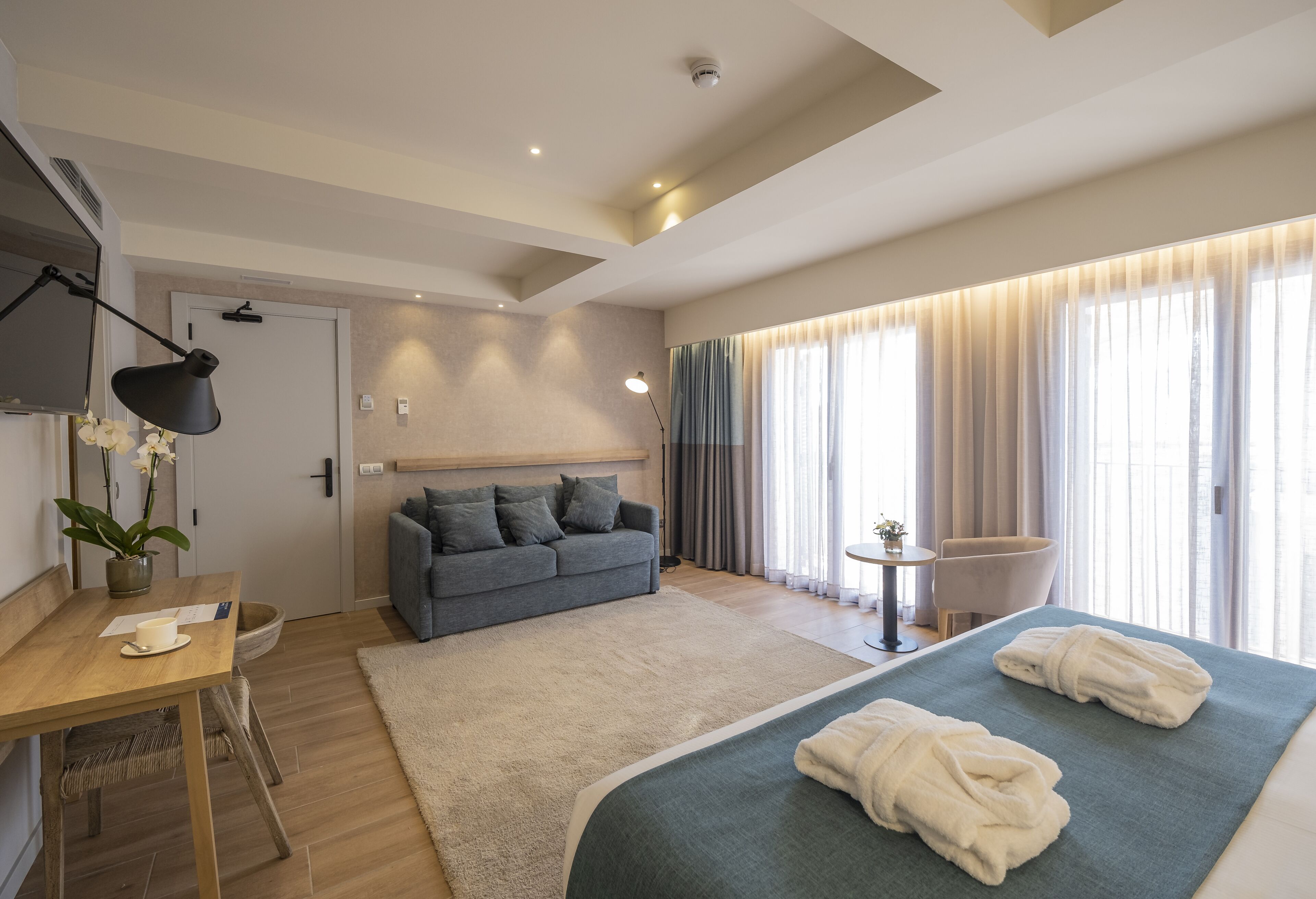 A modern hotel room with a bed, a sofa, a desk, and a chair.