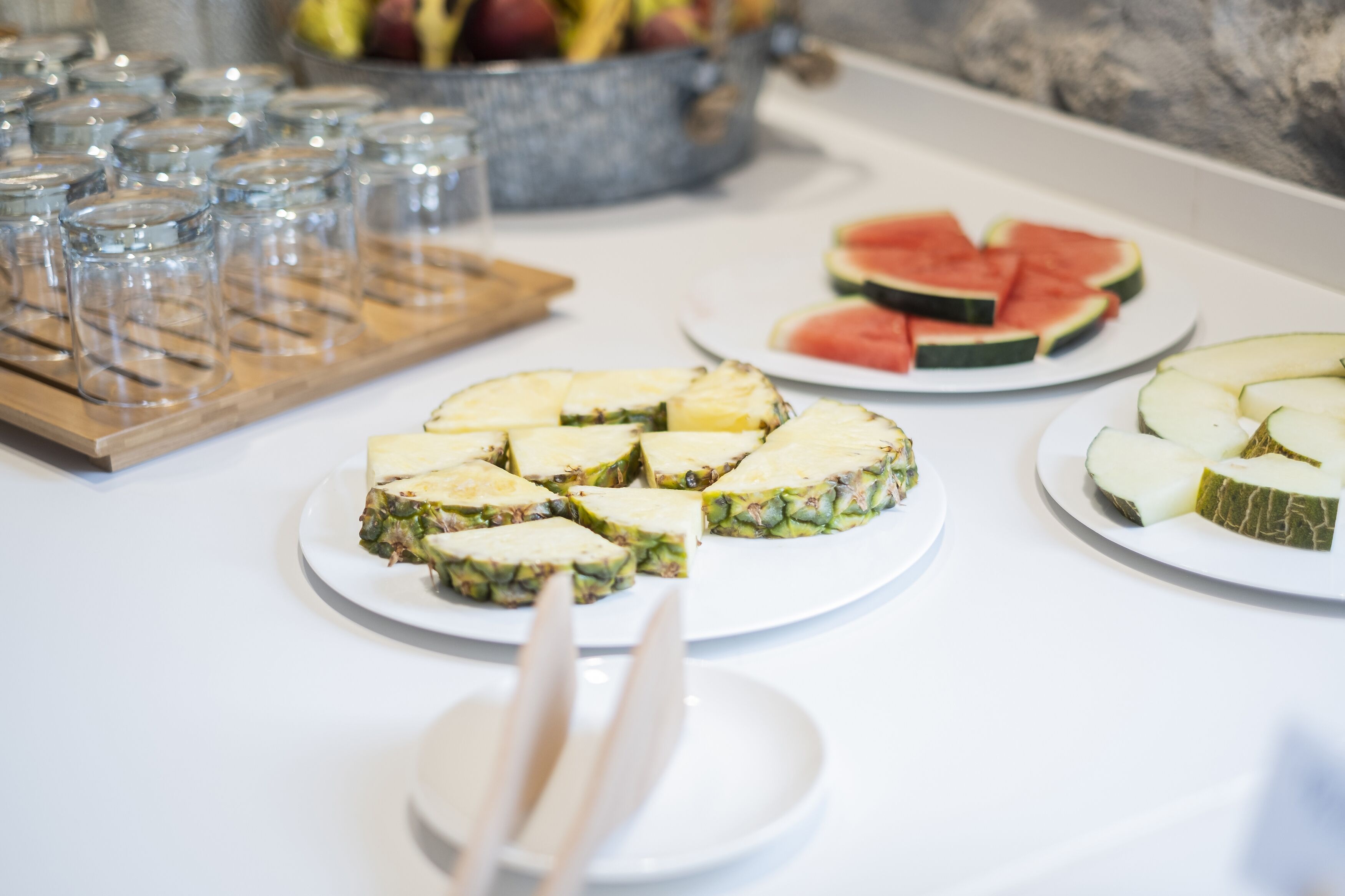 Une table de buffet proposant divers plats, notamment des tranches de pastèque et d’ananas.