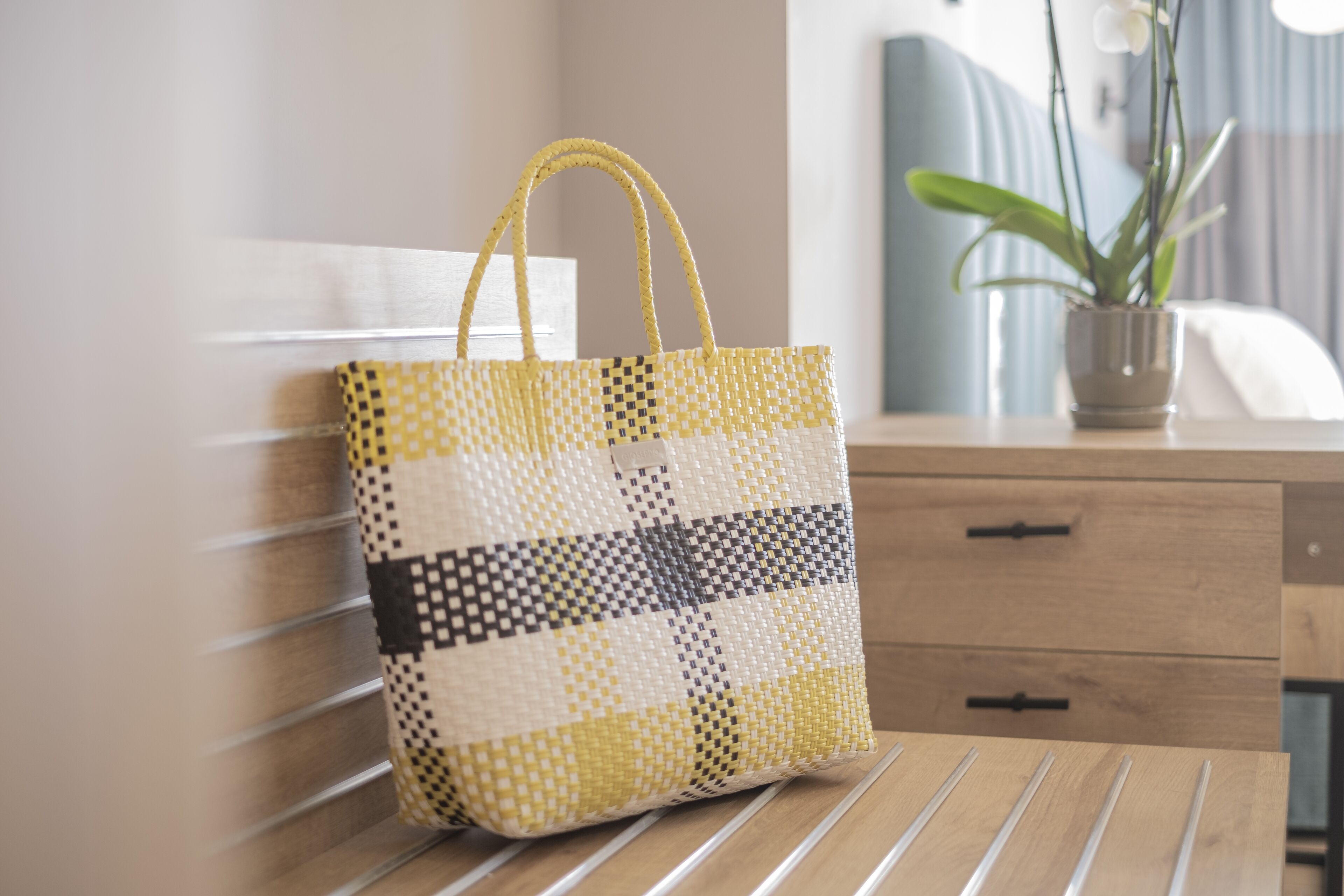 Un sac fourre-tout à carreaux posé sur un banc en bois dans une chambre d’hôtel.