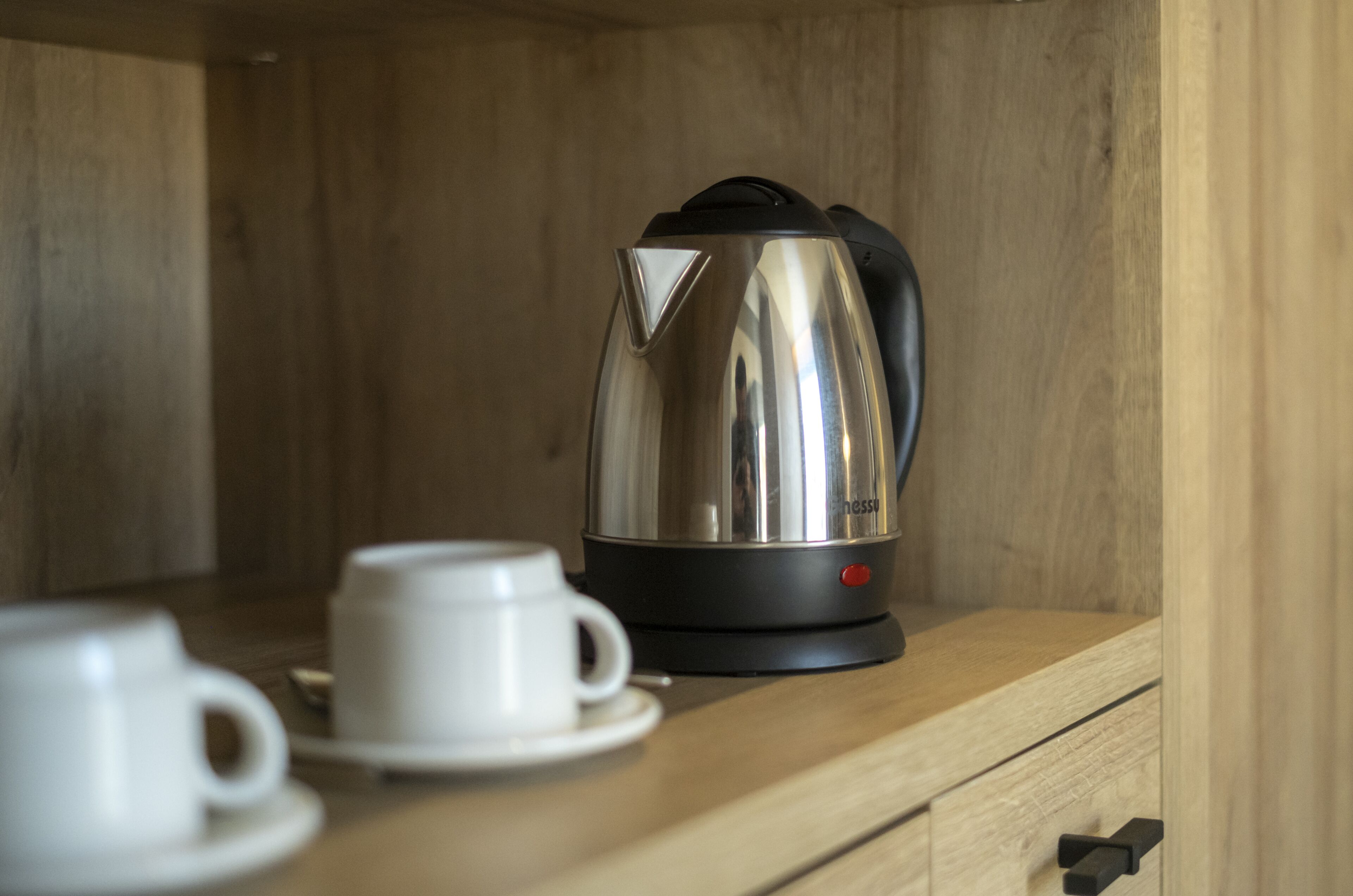 Une machine à expresso en acier inoxydable, posée sur un comptoir en bois, avec une tasse et une soucoupe blanches à côté.