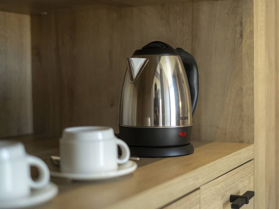 Une machine à expresso en acier inoxydable, posée sur un comptoir en bois, avec une tasse et une soucoupe blanches à côté.