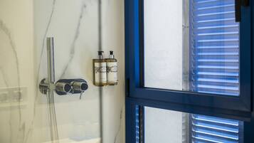 A bathroom with a shower, a marble wall, and two bottles of lotion on the wall.