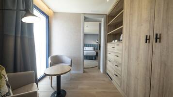 A modern hotel room with a round table, a sofa, a wardrobe, and a bed in the background.