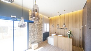 A modern reception area with a stone wall, wooden paneling, and a reception desk. - Hotel Voramar (L'Escala)