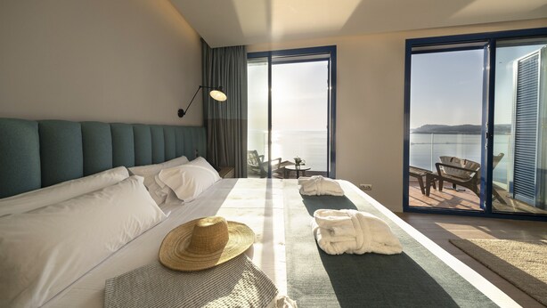 A hotel room with a large bed, a view of the sea, and a balcony with outdoor furniture. - Hotel Voramar (L'Escala)