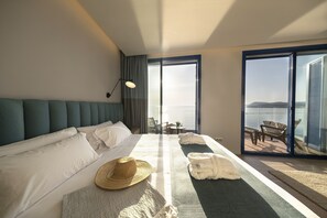 Habitación de hotel con una cama grande, vistas al mar y un balcón con mobiliario exterior.