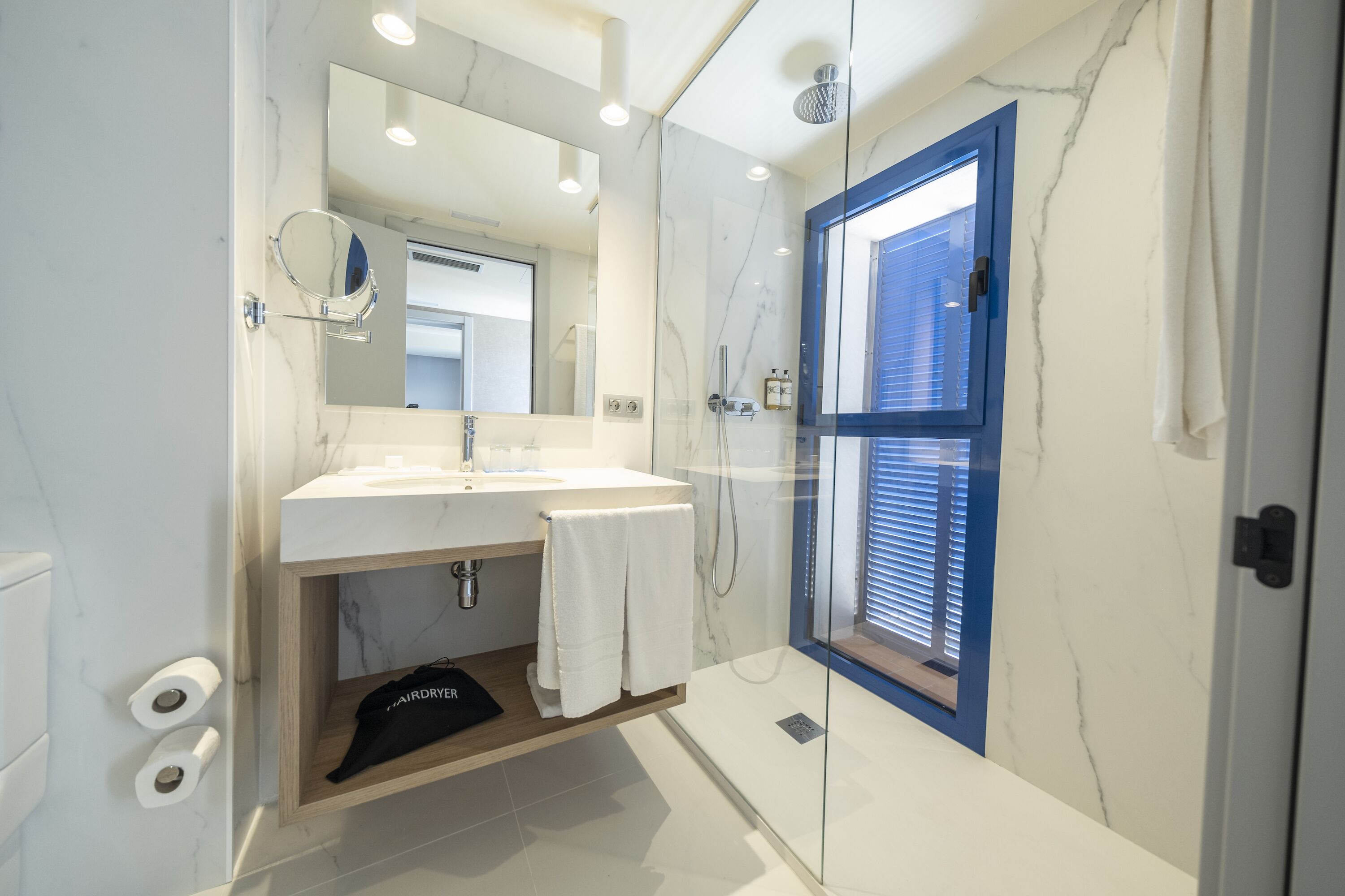 Une salle de bain moderne avec un lavabo en marbre, une cabine de douche en verre et une fenêtre à cadre bleu.