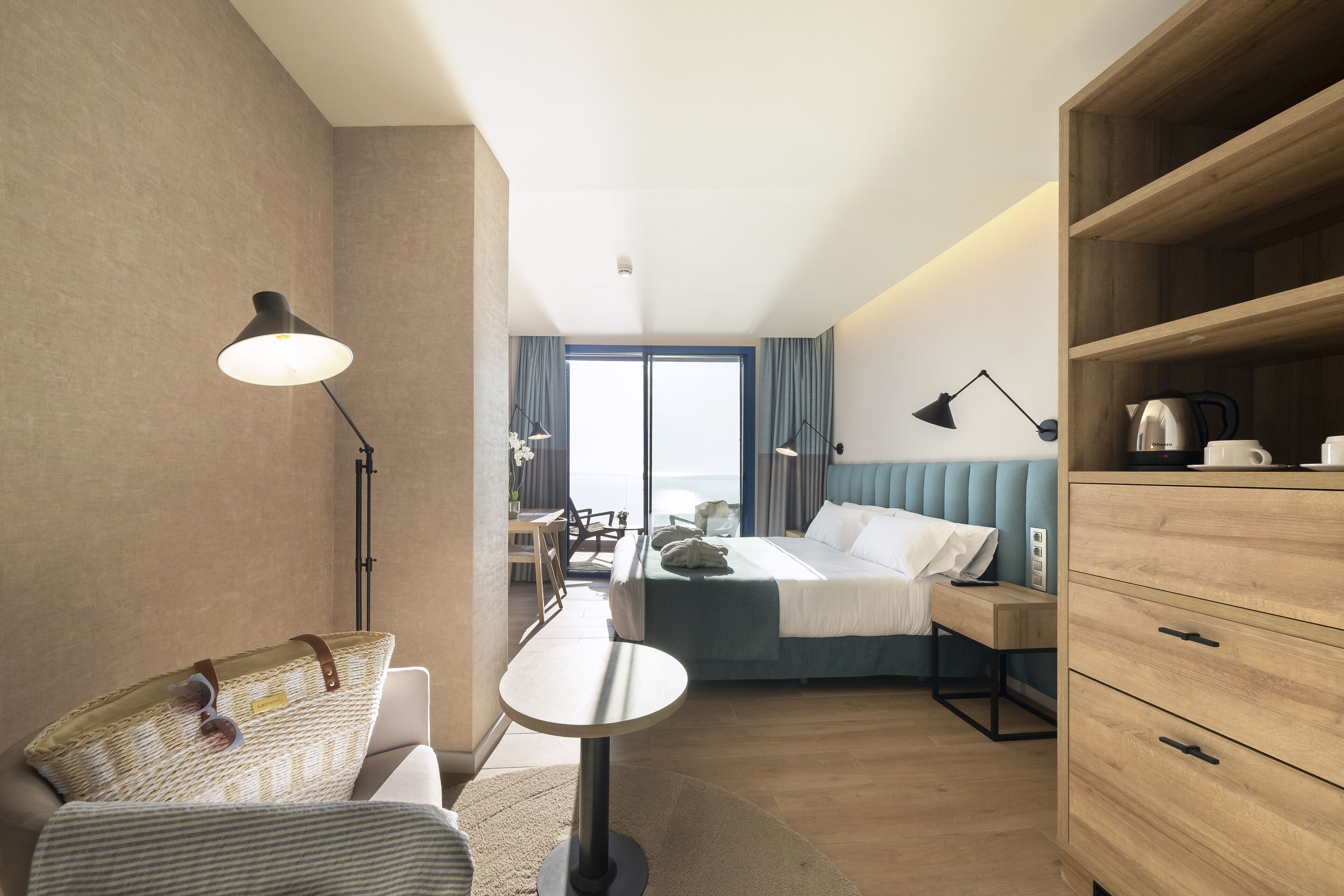 Moderni hotellihuone, jossa on sänky, yöpöytä, lamppu ja näkymä merelle.