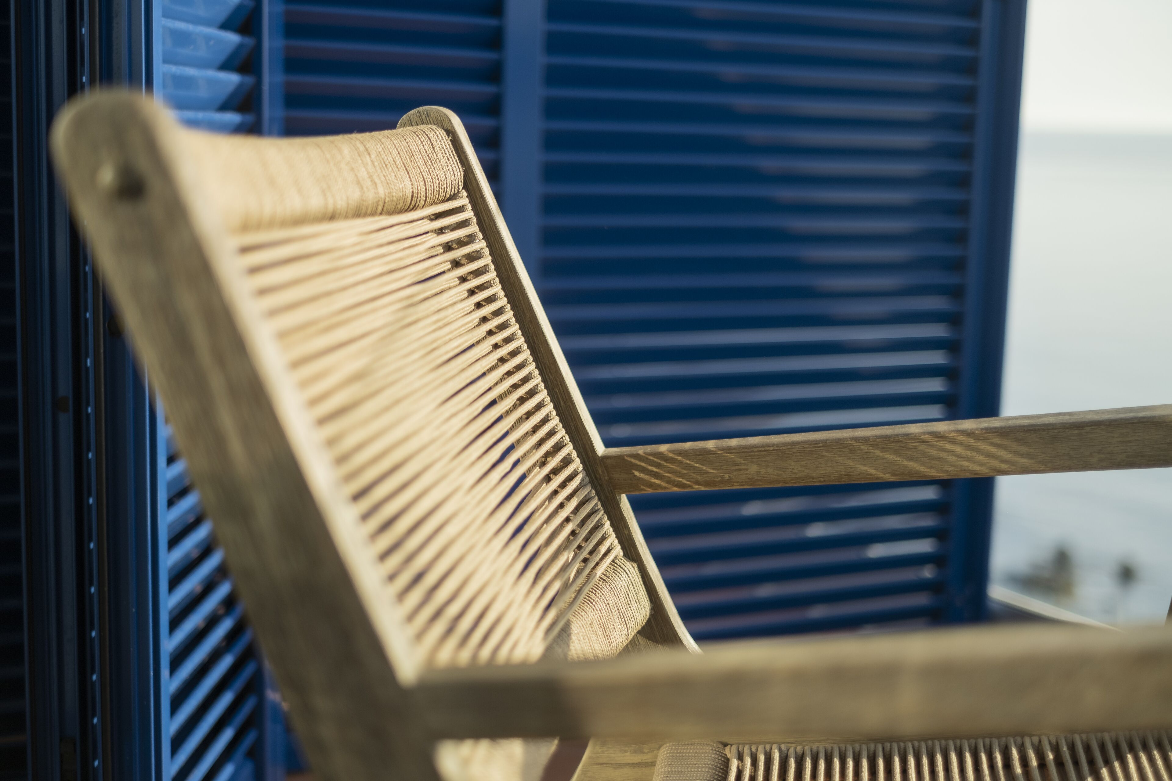 Una silla de madera con respaldo trenzado, ubicada frente a una ventana con contraventanas azules.