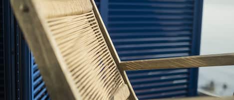 A wooden chair with a woven backrest, positioned in front of a window with blue shutters.