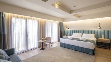 Una habitación de hotel moderna con una cama grande, una zona de estar con una silla, una mesita y una mesita de noche con lámpara.