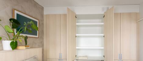 A bedroom with a bed, a wardrobe, a shelf with a plant, and a framed picture on the wall.