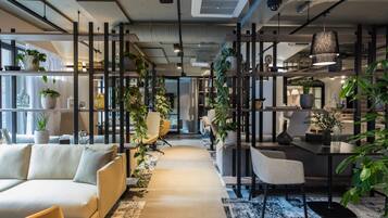 Un espacio de oficina moderno con un sofá, sillas, una mesa de comedor y plantas en macetas.