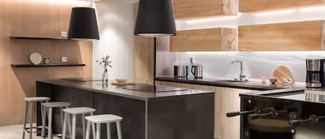 Una cocina moderna con una isla central, taburetes de bar, lámparas colgantes y paneles de madera en la pared.
