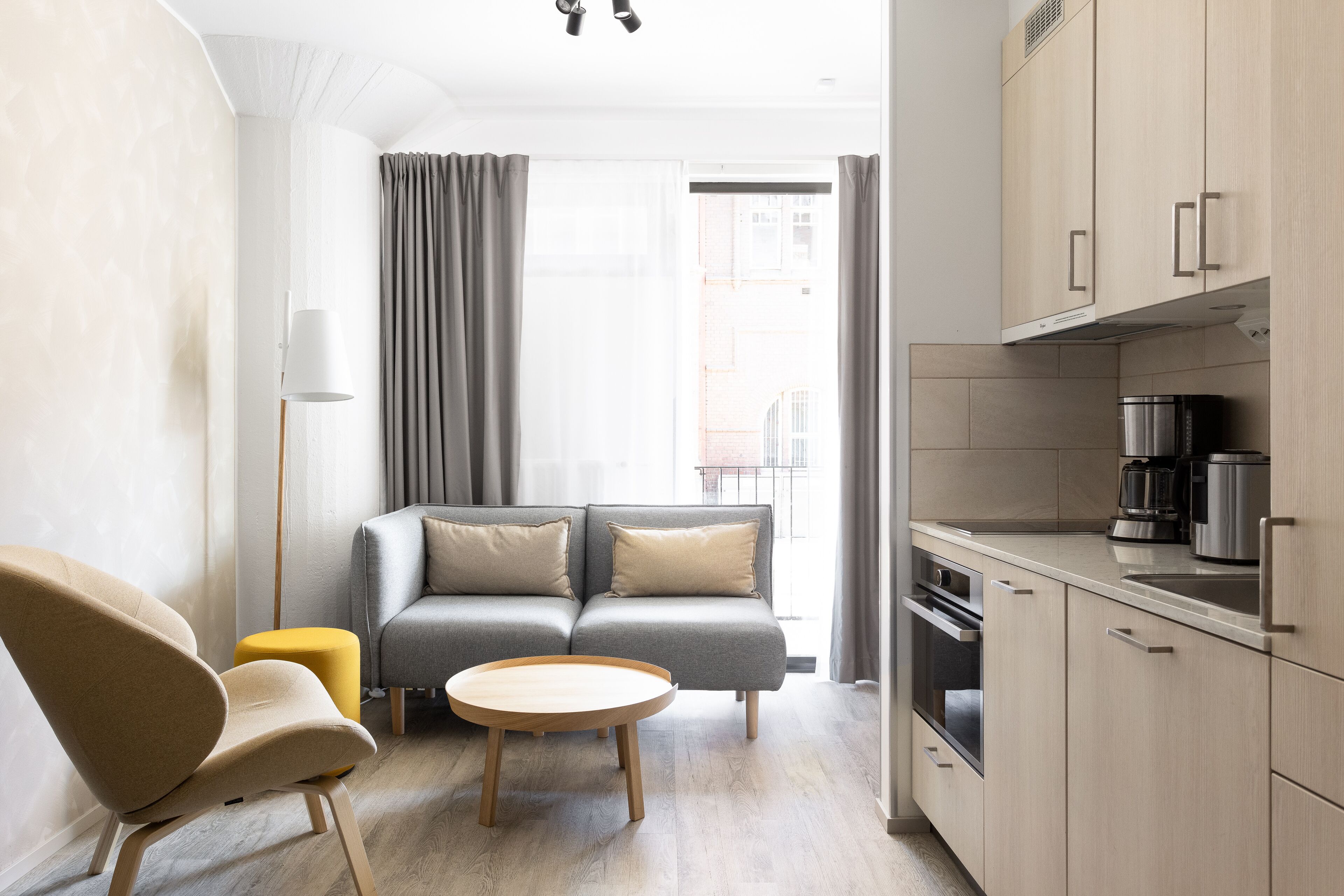 A modern living room with a sofa, a coffee table, and a chair. There is a kitchen area with cabinets and appliances.