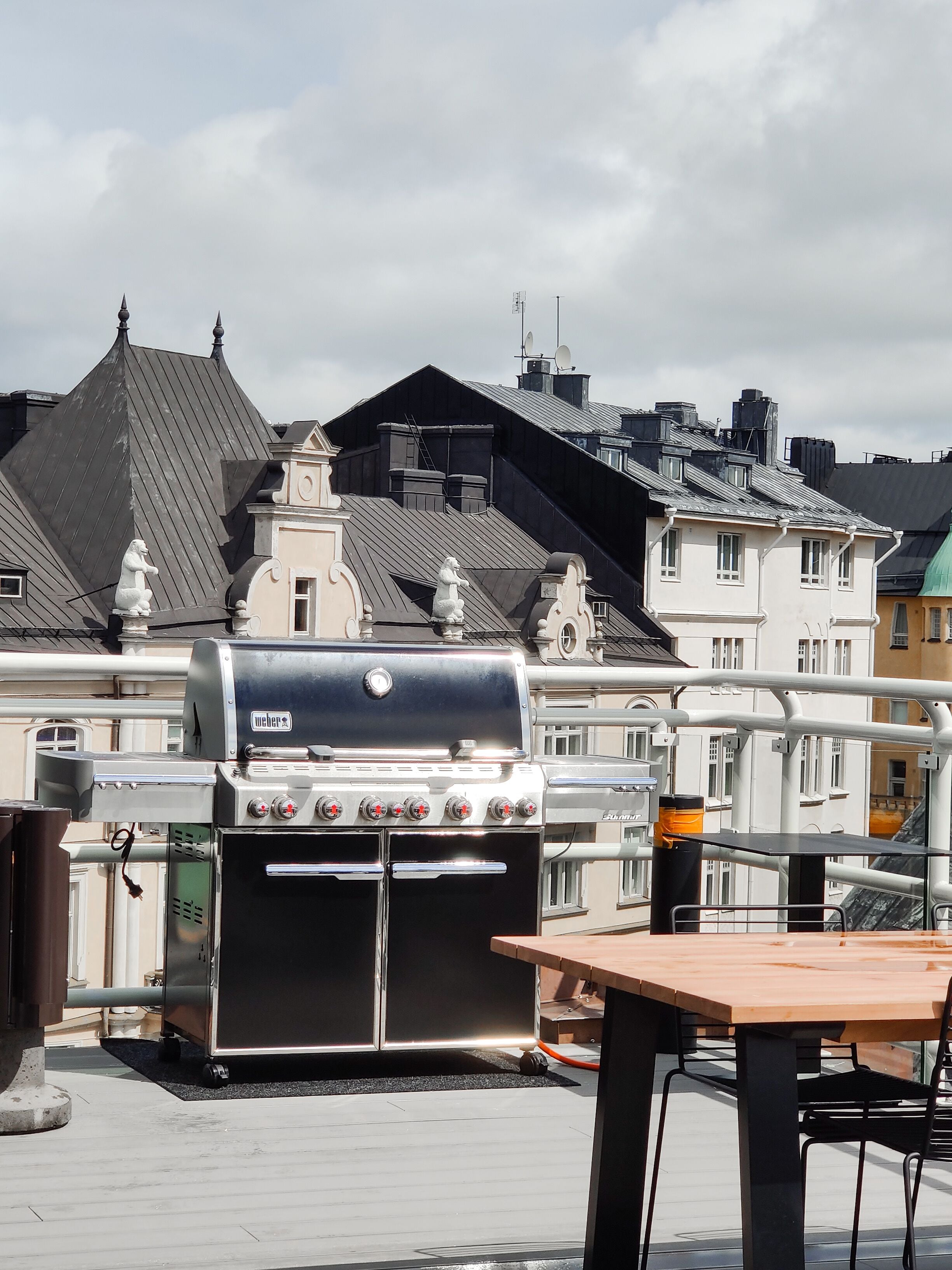 Terraço com churrasqueira Wehen, mesa e cadeiras, com vista para um horizonte urbano com edifícios tradicionais.