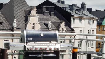 Terraço com churrasqueira Wehen, mesa e cadeiras, com vista para um horizonte urbano com edifícios tradicionais.