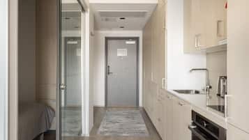 Un corridoio stretto con un letto, una porta e un angolo cottura con pensili ed elettrodomestici.