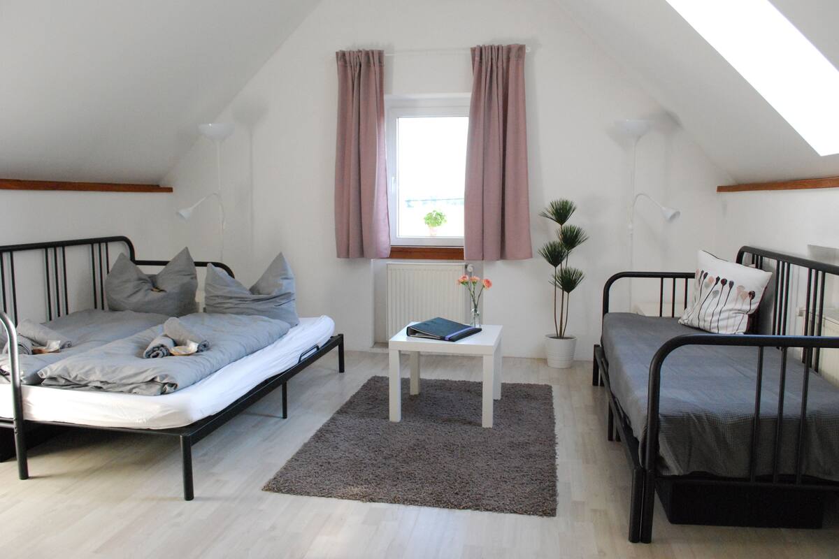 A small, well-lit room with two beds, a small table, and a window with curtains.