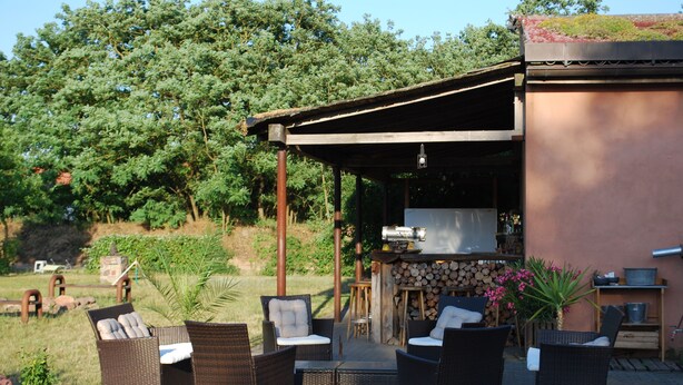 Terrassa exterior amb mobiliari de vimet, una barbacoa i una llar de pedra.