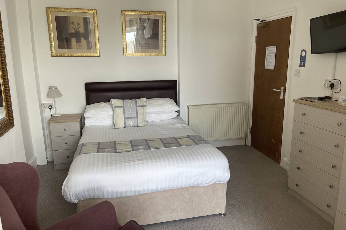 A hotel room with a bed, bedside tables, a dresser, a TV, and framed pictures on the wall.