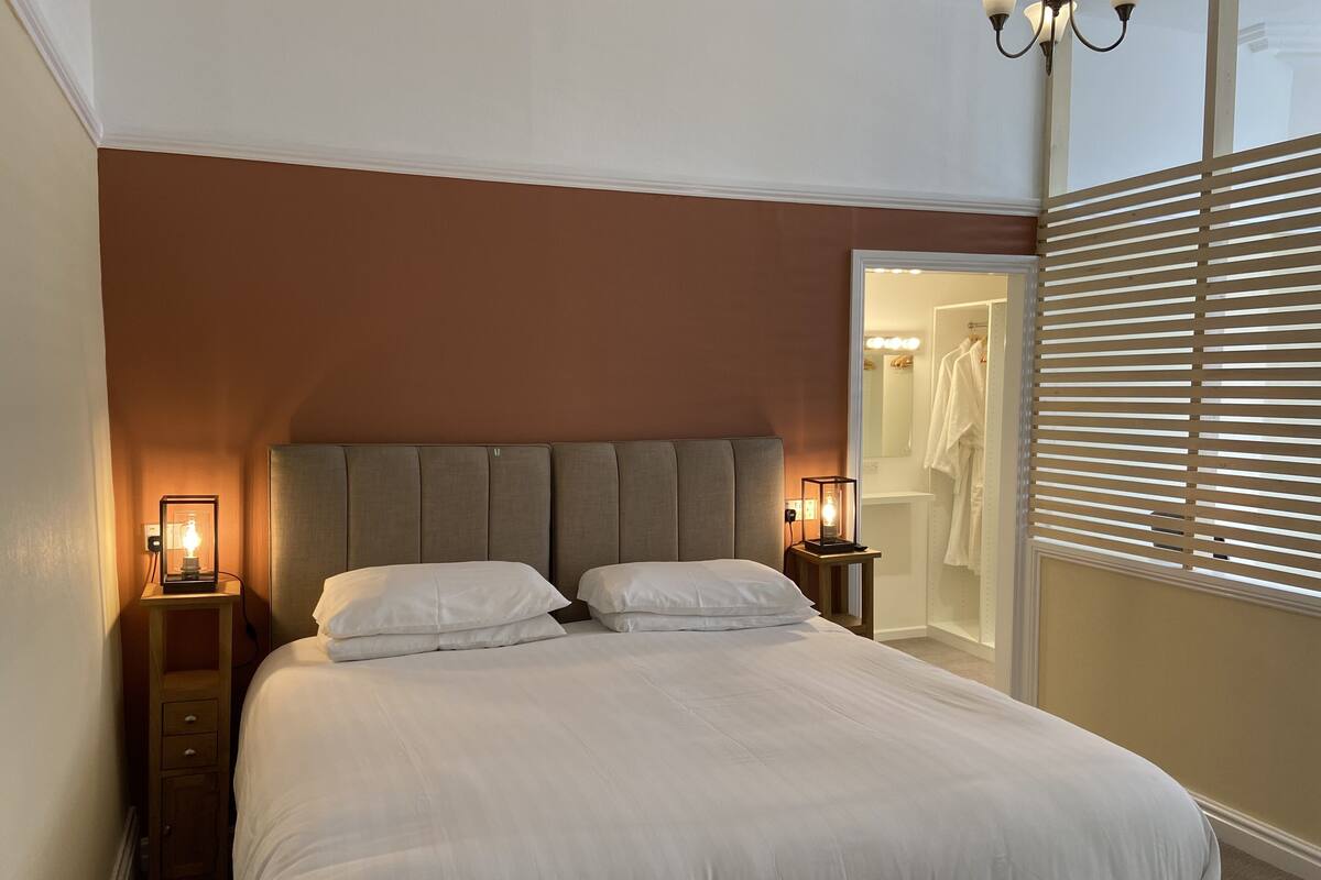A bedroom with a large bed, two bedside tables with lamps, a wardrobe, and a mirror.