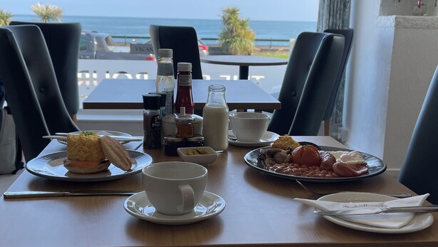 A table set for breakfast with a view of the sea, including plates of food, condiments, and a cup. - The Shelbourne (Llandudno)
