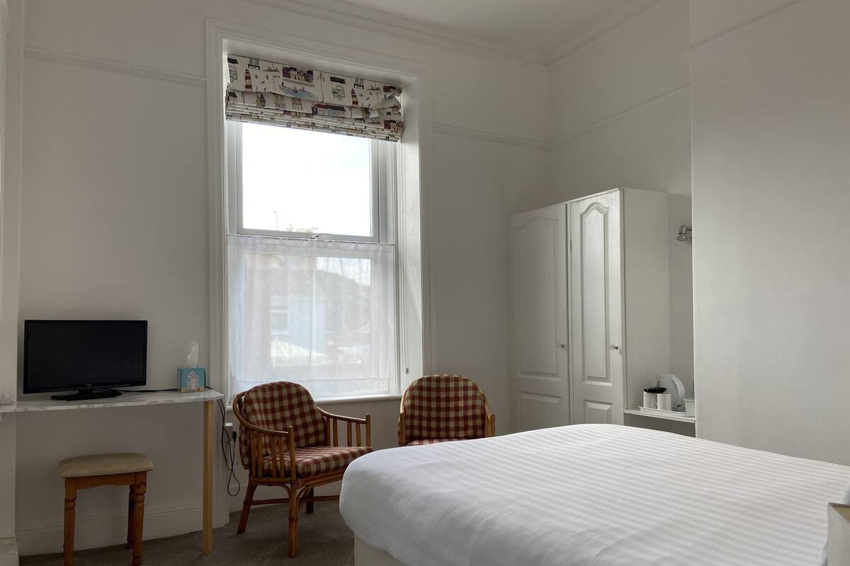 A bedroom with a bed, two checkered chairs, a desk with a computer, and a wardrobe.