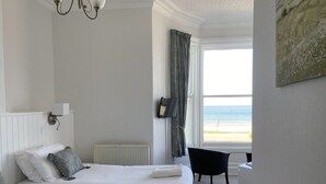 A hotel room with two beds, a view of the beach, a black chair, and a white radiator. - The Shelbourne (Llandudno)