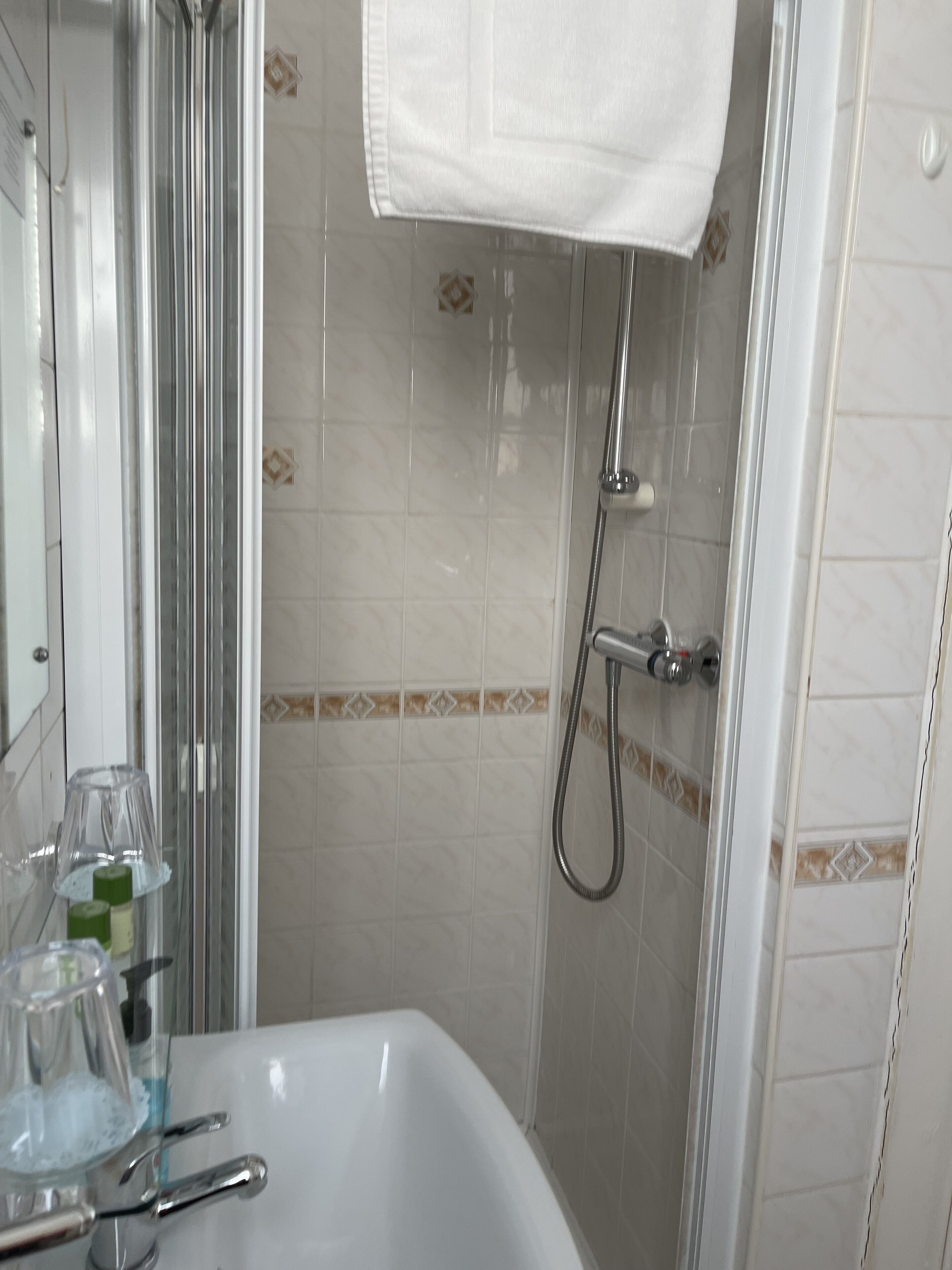 A bathroom with a white sink, glass soap dispenser, and a shower area with a handheld showerhead.