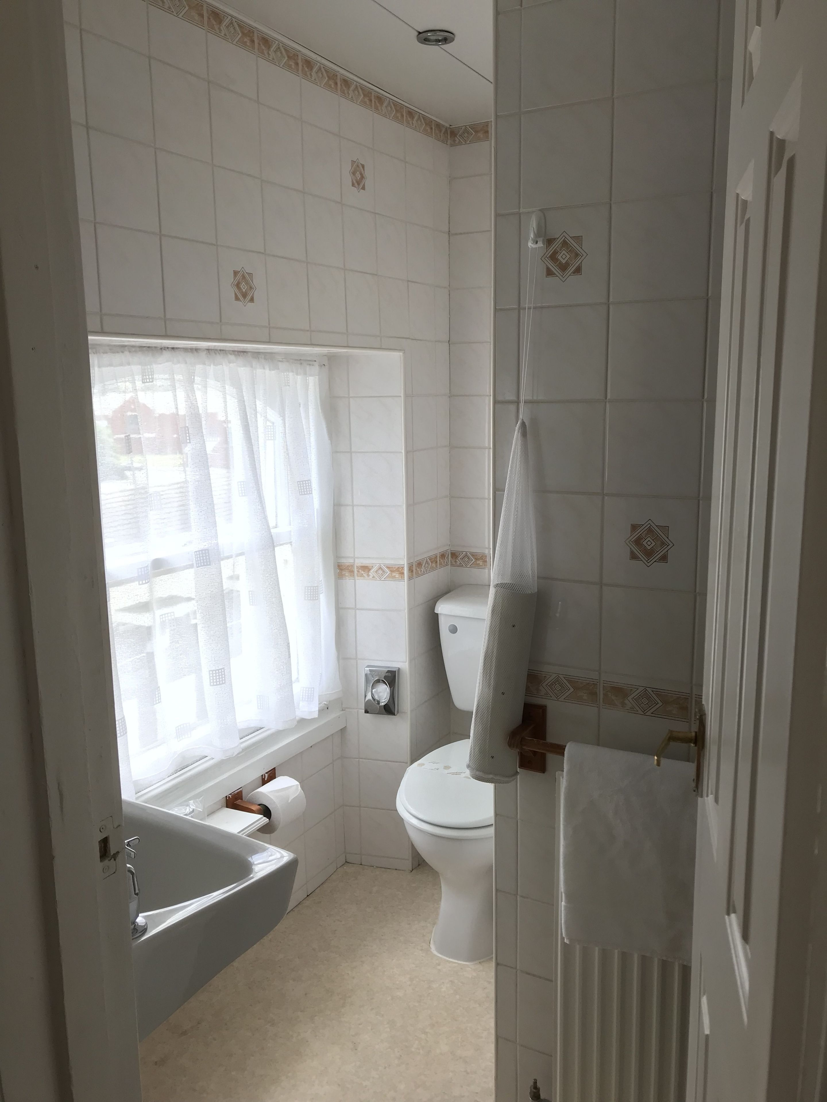 Une salle de bain avec une baignoire, des toilettes et une fenêtre avec des rideaux.