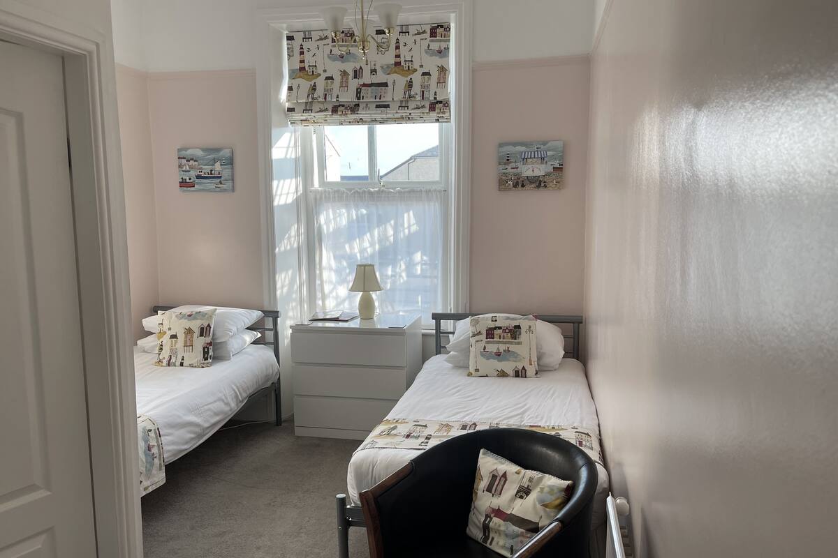 A bedroom with two beds, a chair, a nightstand, and a window with curtains.
