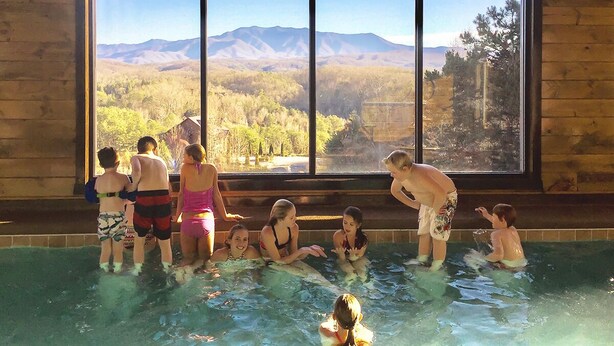 Un grupo de personas en una piscina con vistas a montañas a través de amplias ventanas.