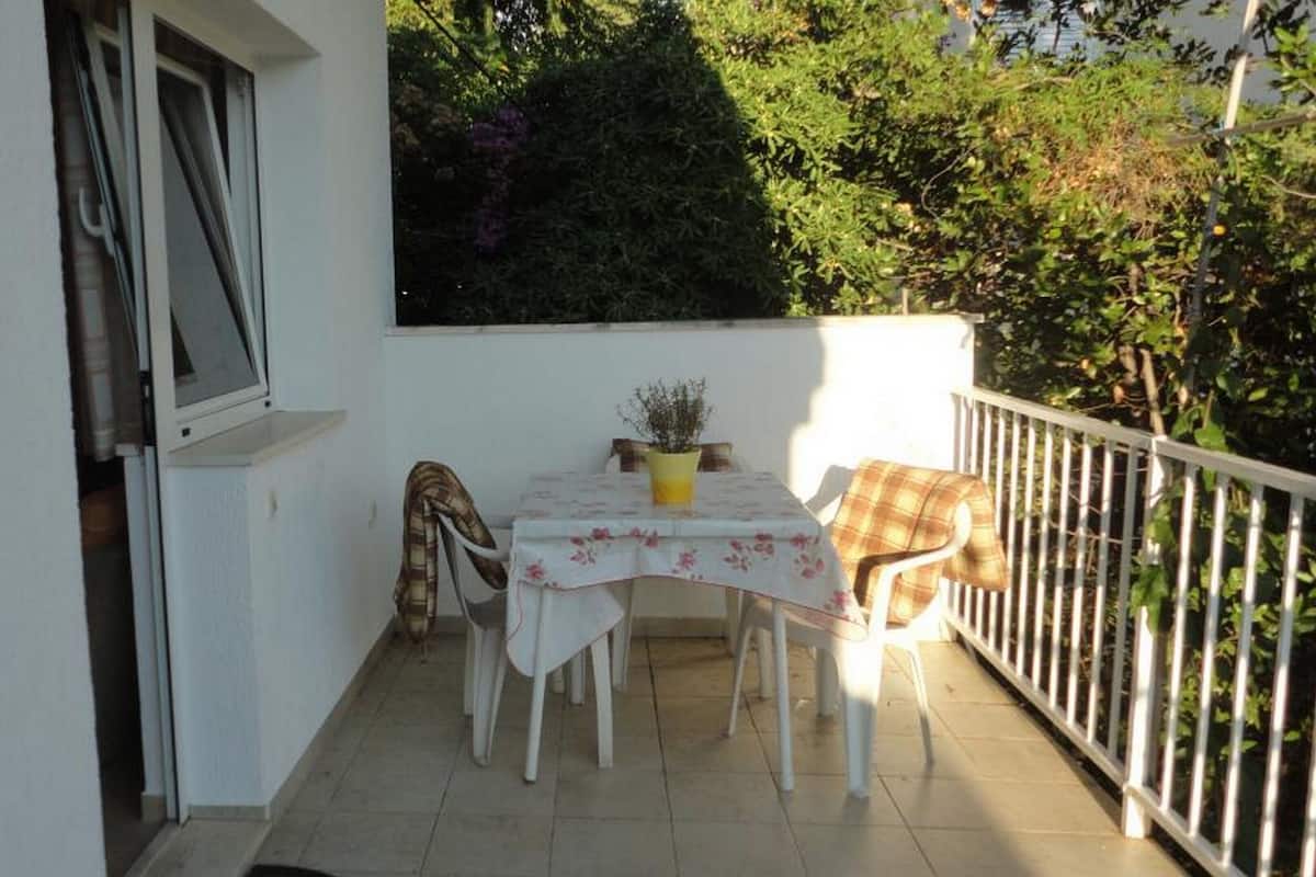A small balcony with a table and chairs, a potted plant, and a white railing.