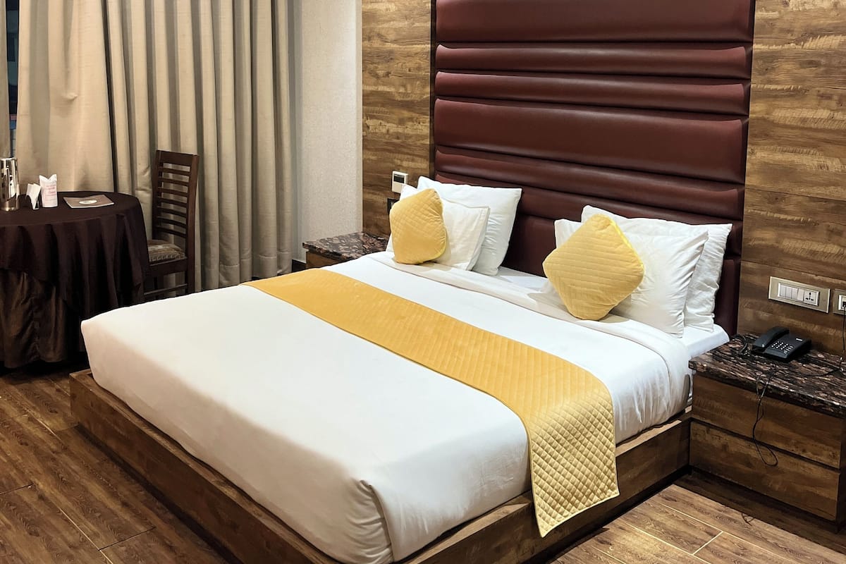 Ein modernes Hotelzimmer mit einem großen Bett, Holzboden, einem dunklen Kopfteil und einem kleinen Tisch mit Telefon.