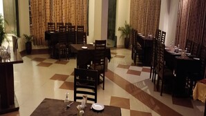 Un restaurant avec de nombreuses tables et chaises, un sol carrelé et des rideaux aux fenêtres.