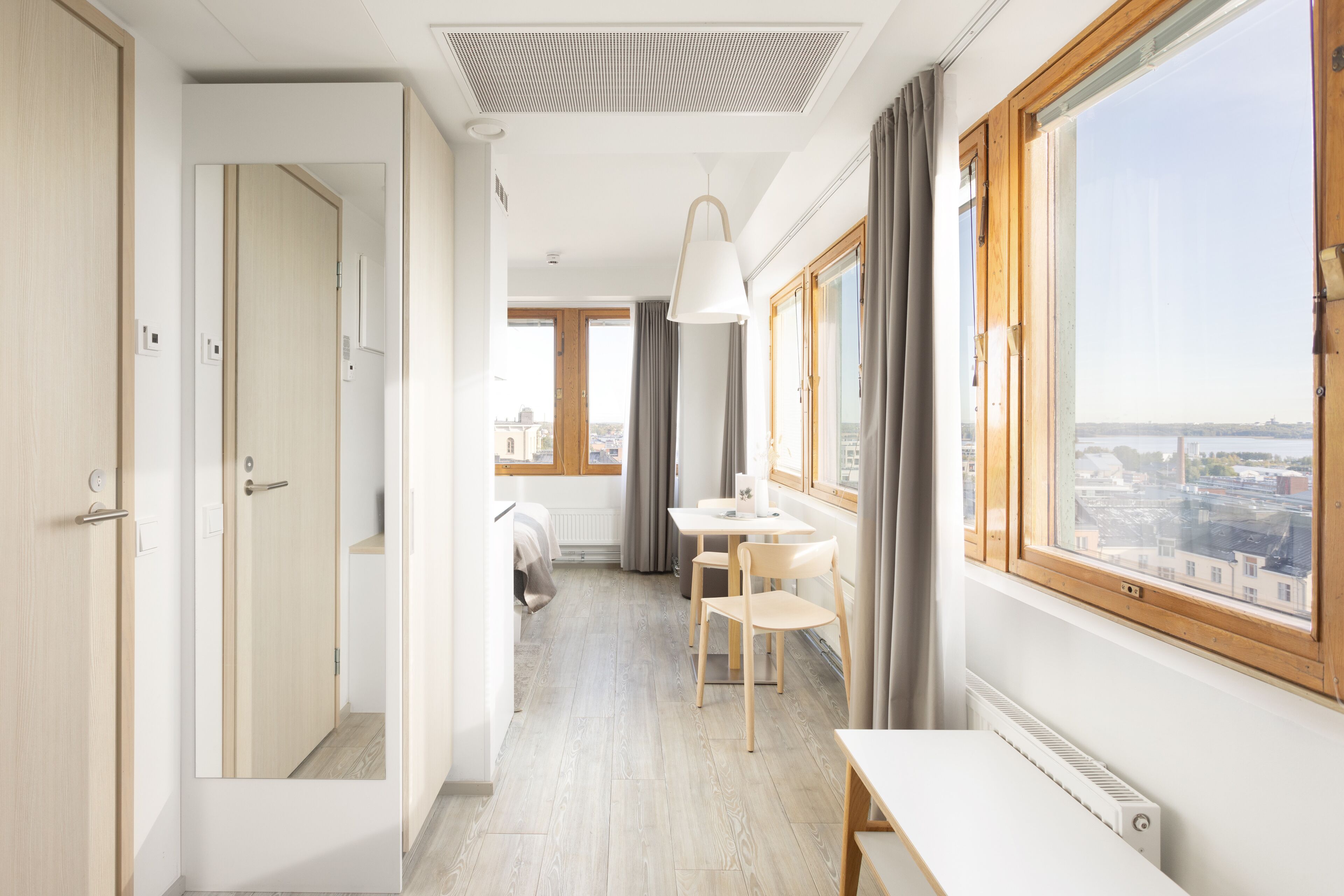 A modern hotel room with a large window, a dining area, and a view of the city.