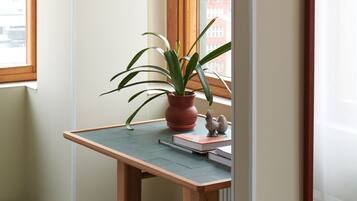 A corner desk with a potted plant and a small figurine, a stool, and a framed picture on the wall.