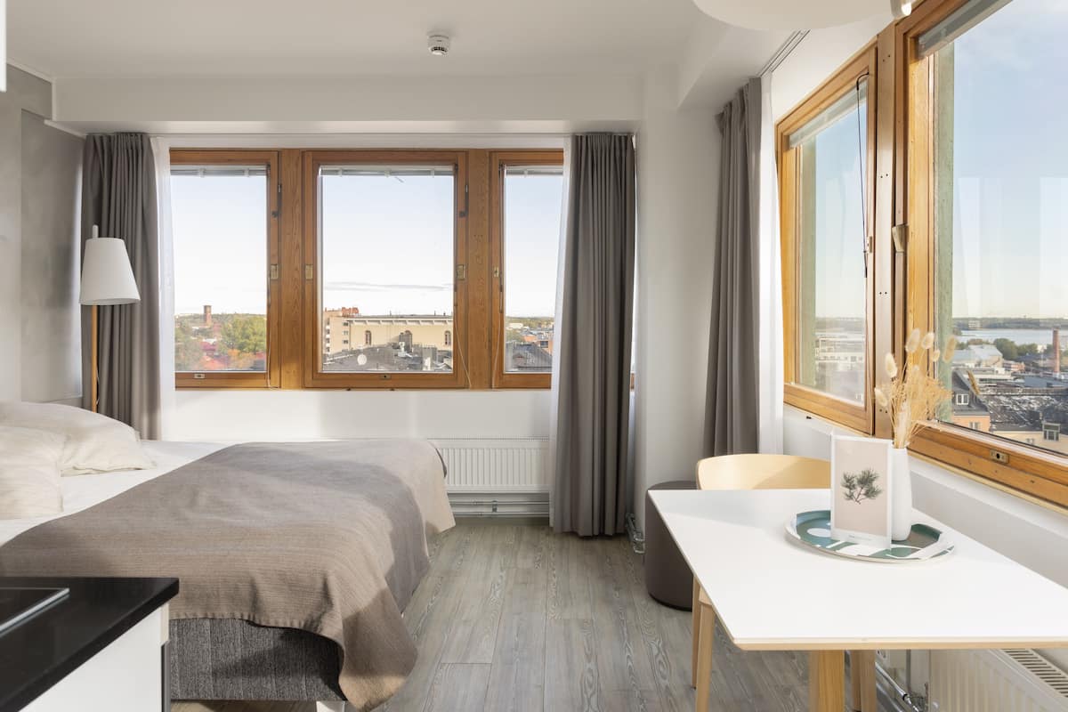 Une chambre d’hôtel avec un lit, un bureau et une vue sur la ville grâce à de grandes fenêtres.