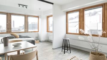 Una habitación moderna y luminosa con amplios ventanales, un comedor con mesa y sillas, y una zona de estar acogedora con sofá y radiador.
