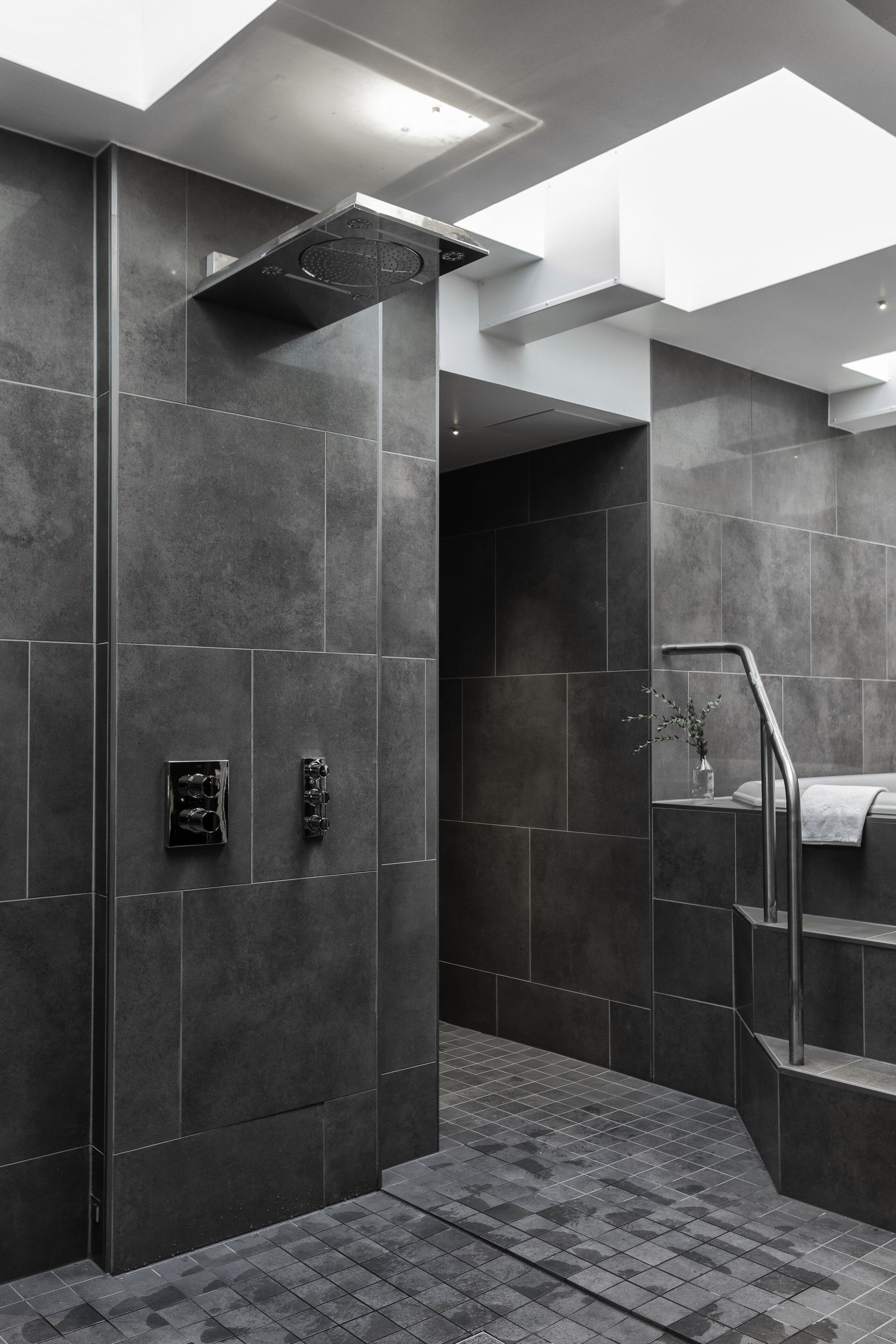 A modern bathroom with dark tiles, a shower area, and a staircase with a towel rack.