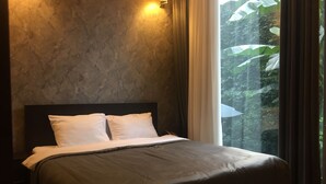 Un dormitorio con cama, cabecera, mesita de noche y ventana con cortinas.
