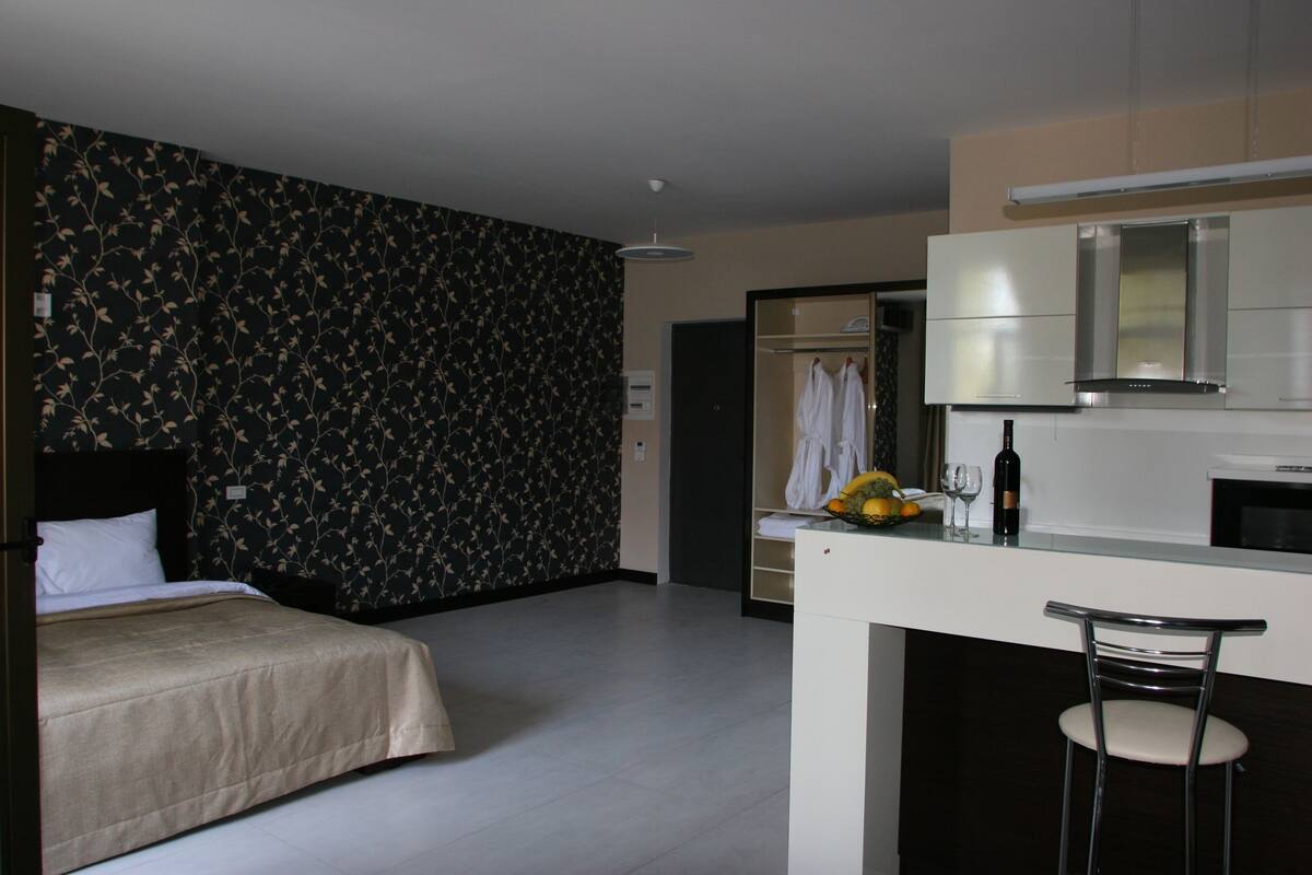 A hotel room with a bed, a small kitchenette, and a bathroom.