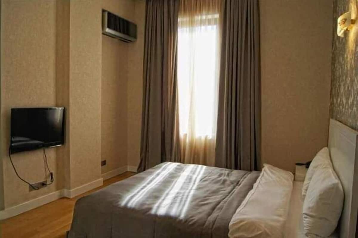 A hotel room with a bed, a flat-screen TV mounted on the wall, and a window with curtains.