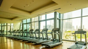 A gym with treadmills aligned in rows, large windows, and a view of a cityscape. - Bravo Way Burj Vista 1 (Dubai)