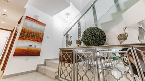 Een moderne trap met glazen leuning, een decoratieve metalen balustrade en een schilderij van een zonsondergang.