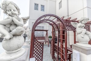 Ein Innenhof mit einer Holz-Pergola, Steinfiguren und Blick auf ein Gebäude mit Fenstern.