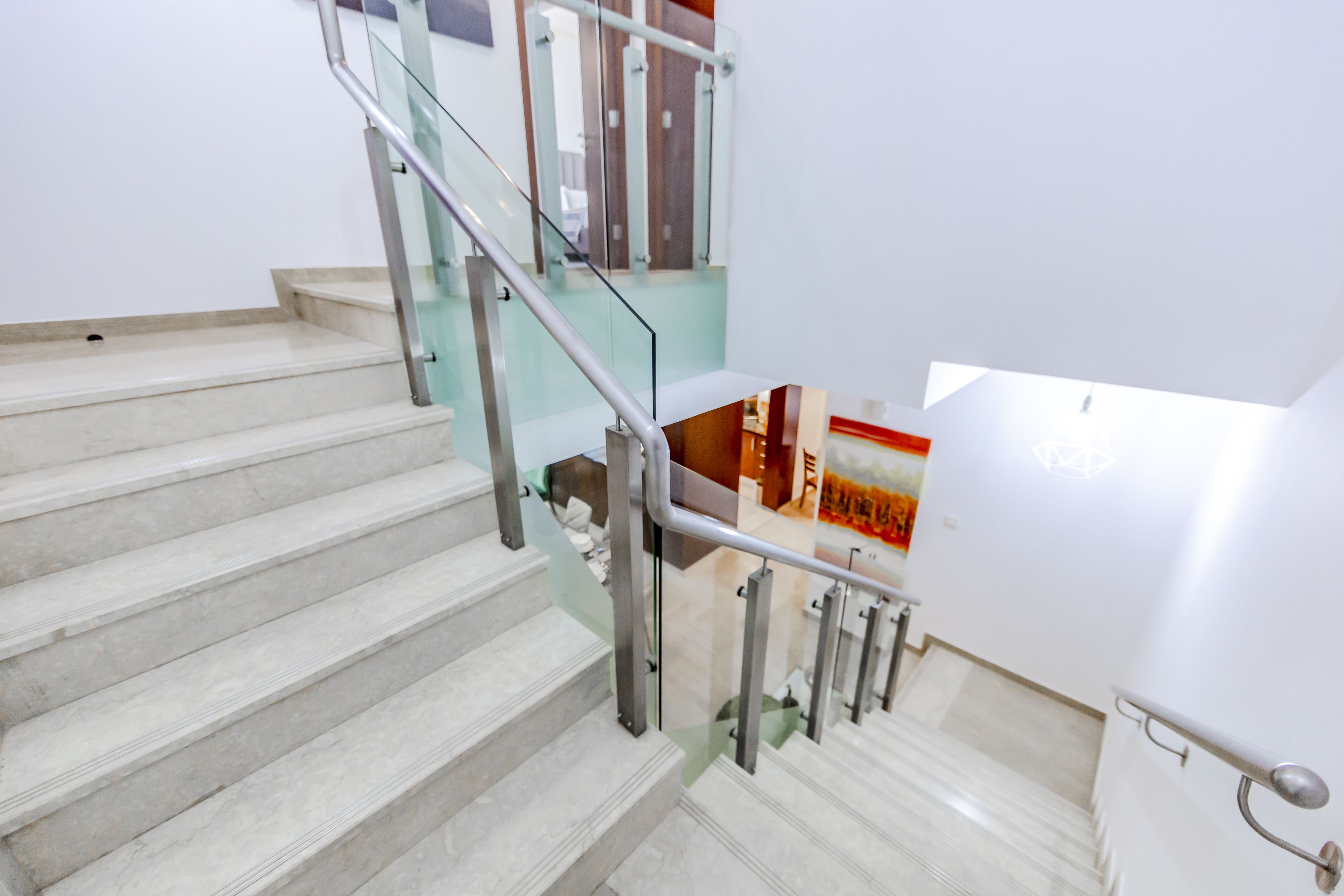 A staircase with glass railings and a white wall.