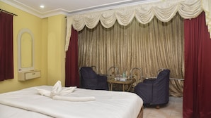 A hotel room with a bed, a mirror, a small table, two chairs, and a curtain. - Hotel Ispat International (Asansol)
