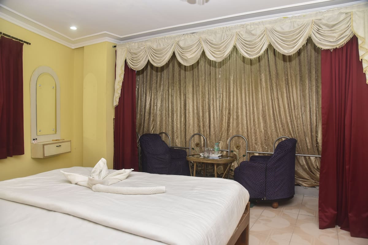A hotel room with a bed, a mirror, a small table, two chairs, and a curtain.